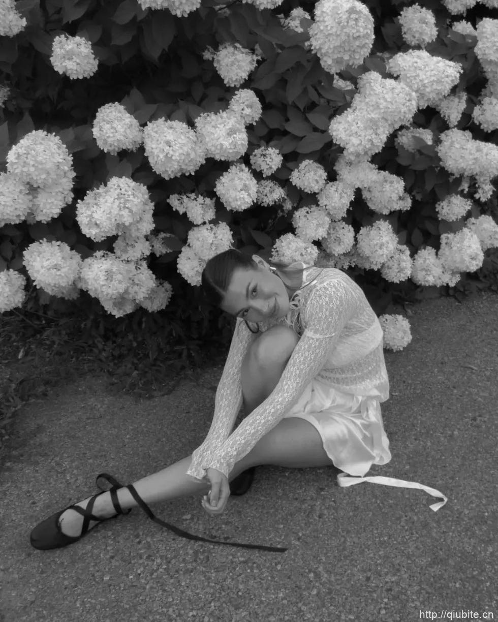 a person sitting on the ground with flowers in the background 为什么2024年了,芭蕾平底鞋还在流行?