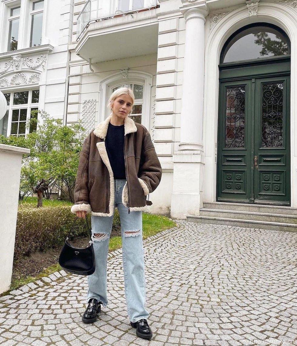 a person standing in front of a building 冬日暖阳下的时髦选择:毛领夹克