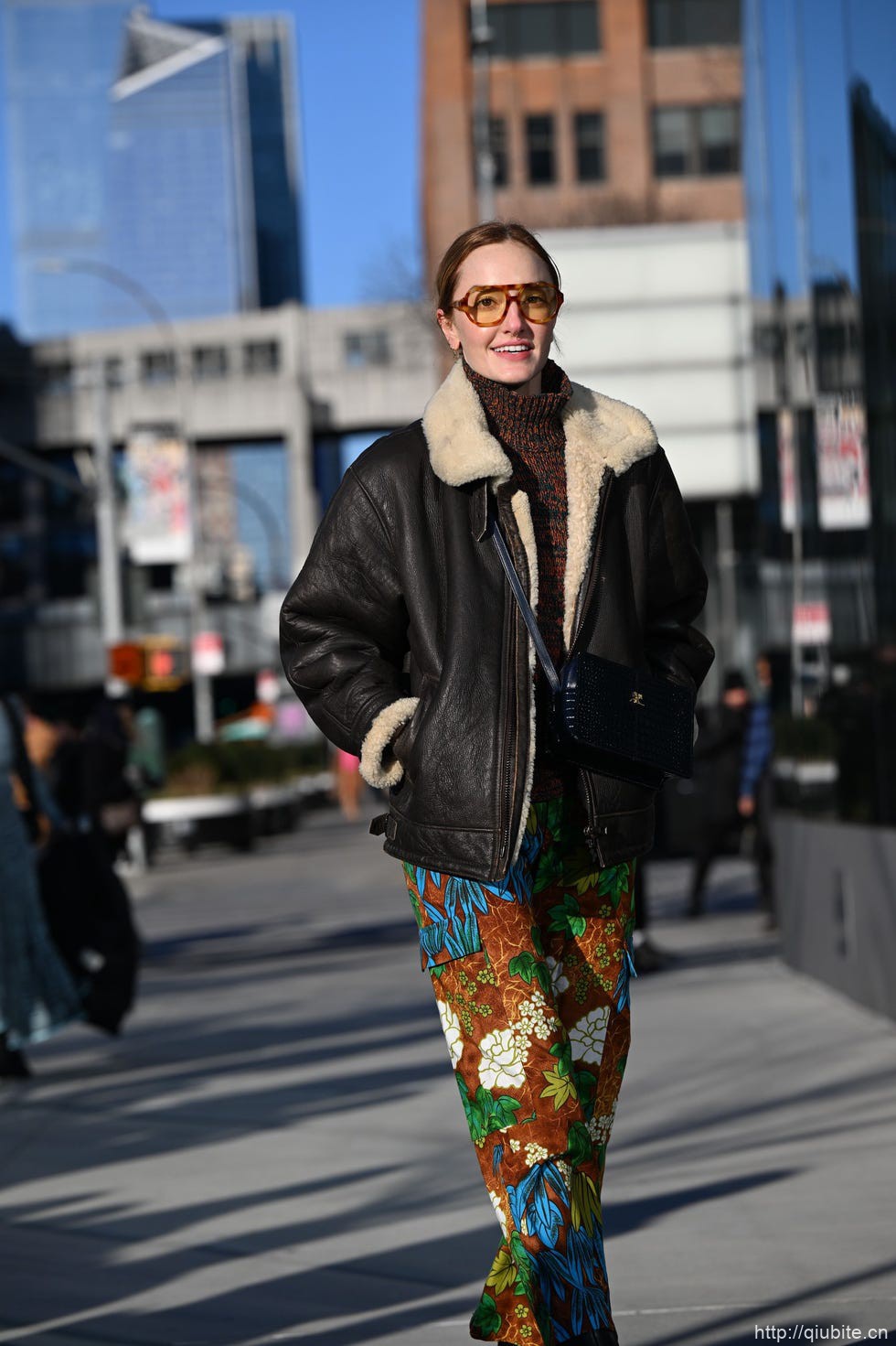 a person in a black coat and scarf walking on a street 冬日暖阳下的时髦选择:毛领夹克